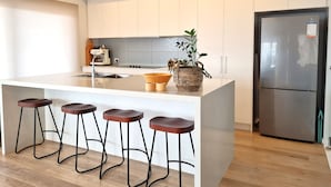 Une cuisine moderne avec des meubles blancs, un îlot central doté de tabourets, une cuisinière encastrée et un réfrigérateur en acier inoxydable.