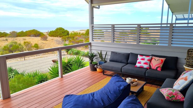 Un espace extérieur aménagé, abrité et doté d’un canapé et de coussins, d’une terrasse en bois et d’une vue sur l’océan et le paysage.