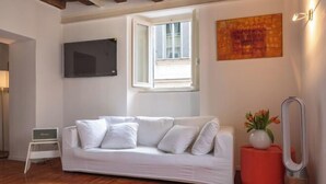 A modern living room with a white sofa, a small table with a vase, a red stool, and a floor lamp. - Casa Cristina in Piazza Farnese (Rome)
