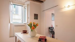 A room with a white table, a vase with flowers, a book, a radiator, a window, and a door leading to another room. - Casa Cristina in Piazza Farnese (Rome)
