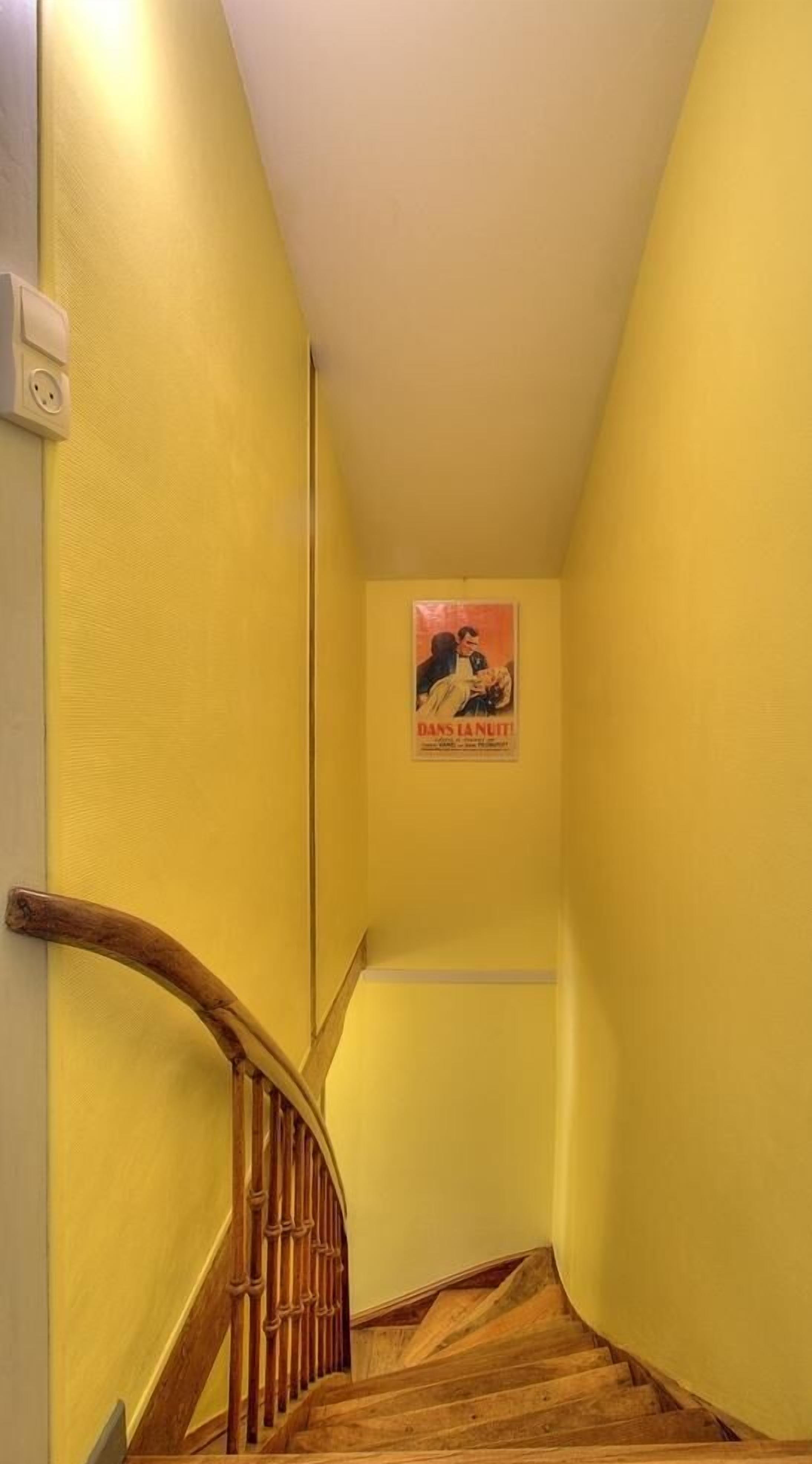 A narrow hallway with yellow walls and a wooden staircase.