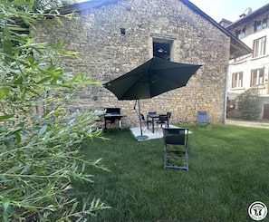 Ein SteingebĂ€ude mit einer Terrasse, ausgestattet mit einem Tisch, StĂŒhlen und einem groĂen Sonnenschirm.