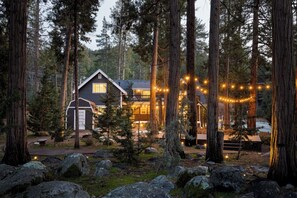 Une cabane entourée de grands arbres, illuminée de guirlandes lumineuses.