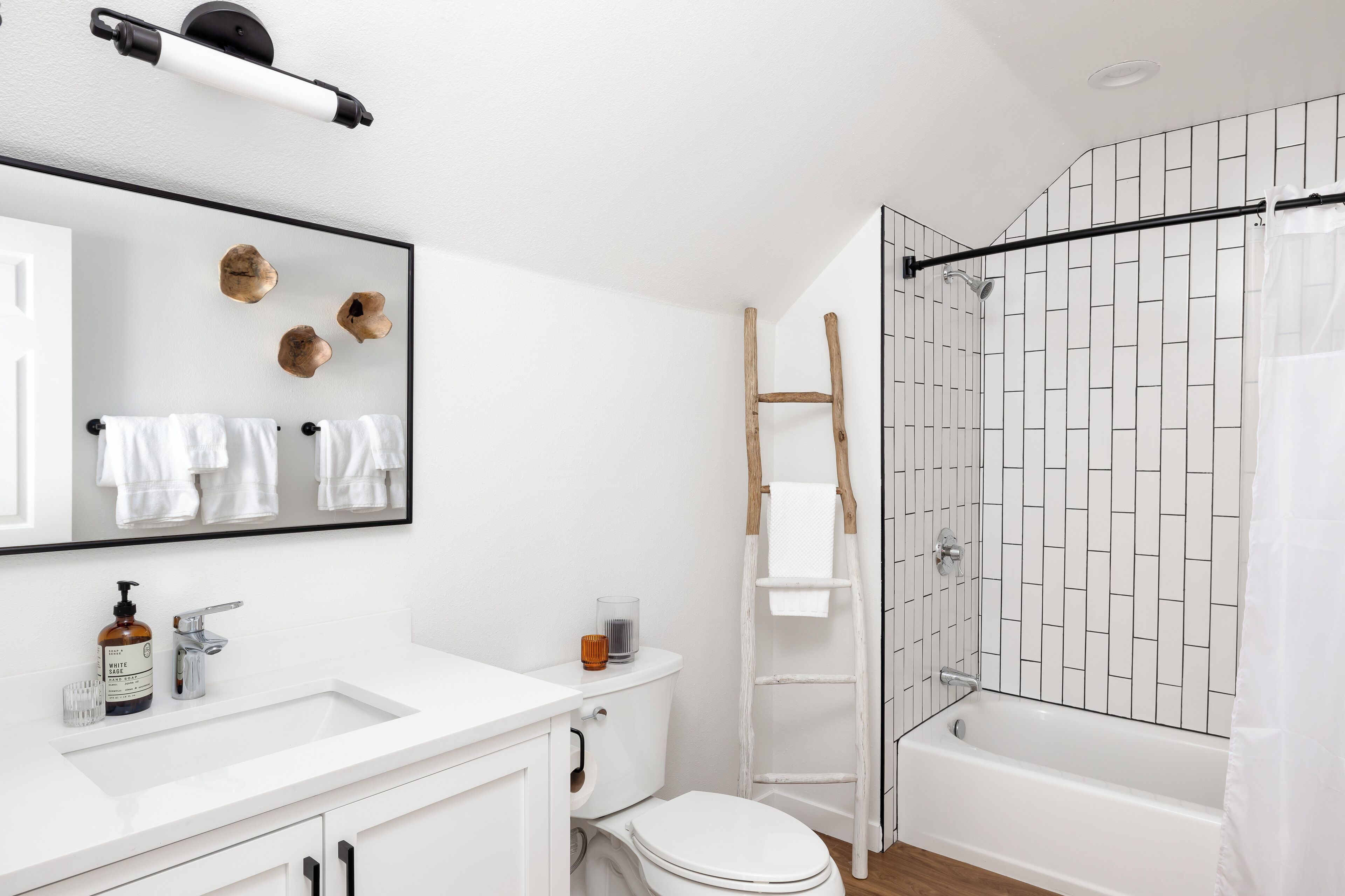 A modern bathroom with a white sink, mirror, and toilet. There is a shower area with a glass door and a wooden ladder.