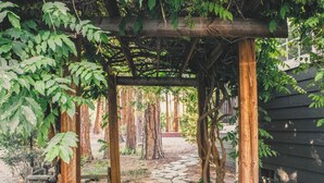 A stone pathway leading through a wooden pergola structure surrounded by trees and a wooden building. - Harvey House (Idyllwild)