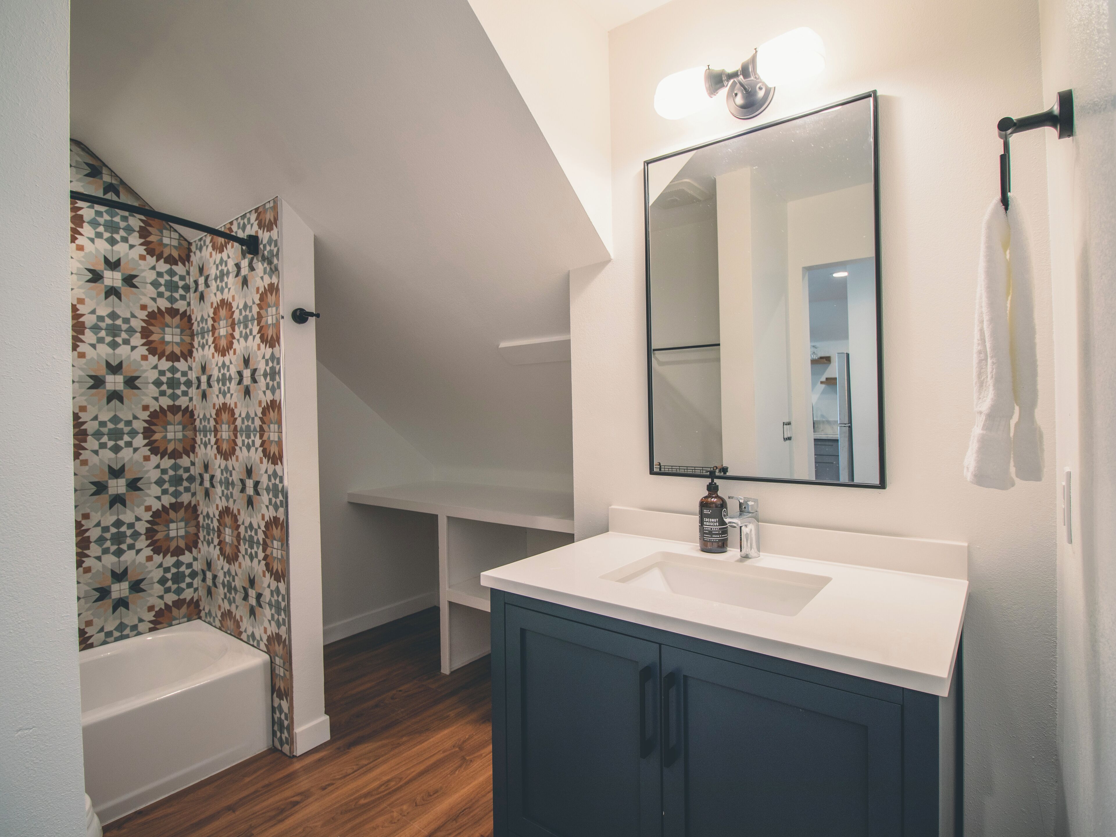 A bathroom with a white bathtub, a sink with a mirror above it, and a shower curtain with a geometric pattern.