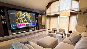 Een moderne woonkamer met een grote flatscreen televisie, een beige bank, een salontafel en een bijzettafeltje.