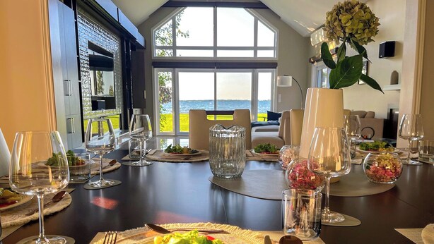 Een eettafel gedekt voor een maaltijd, met uitzicht op zee door grote ramen.