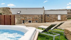 A stone building with a hot tub and lounge chairs in the foreground. - Awel y Môr - 3 Bedroom Cottage - Whitesands (Saint Davids)
