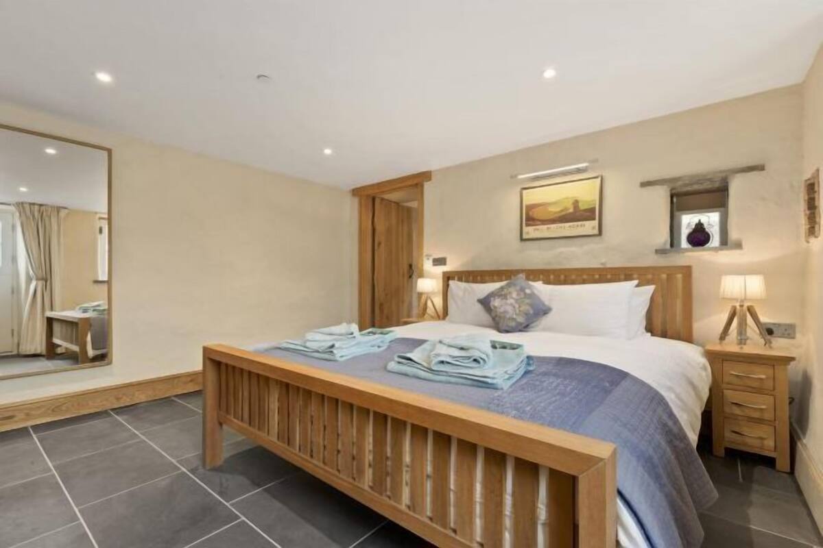 A bedroom with a wooden bed, a nightstand, a mirror, and a wall-mounted picture.