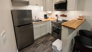 A compact kitchen with white cabinets, a stainless steel refrigerator, a microwave, a stove, and a sink. - Back Beach Retreat - Car Rental Option (Sitka)