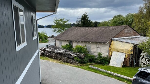 A residential street with a grey house, a wooden deck, and a parked SUV. - Back Beach Retreat - Car Rental Option (Sitka)
