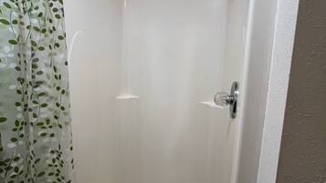 A corner shower with a white tiled wall, a showerhead, and a drain.