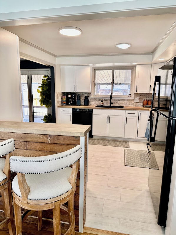 A modern kitchen with white cabinets, a black refrigerator, and a wooden dining table with two chairs. - Homebase 4BR/3BA, Park, Fire-pit, Gym Equip, Theatre, Kids Room, Arcade, AC (Centennial)