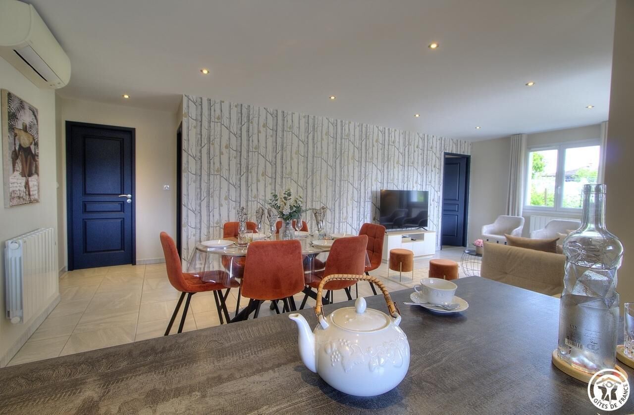 Un coin repas moderne avec une table en bois, des chaises rouges et une théière blanche.