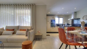 A modern living room with a sofa, a dining table with chairs, and a kitchen in the background.