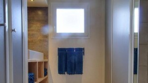 A narrow hallway with a window, a shelf with folded items, and a trash bin.