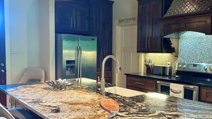 Una cocina con una isla grande, gabinetes de madera oscura, electrodomésticos de acero inoxidable e iluminación colgante.