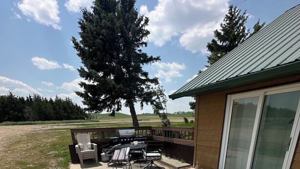 An outdoor patio area with a grill, seating, and a view of a grassy field and trees. - Rustic Ridge (Gregory)