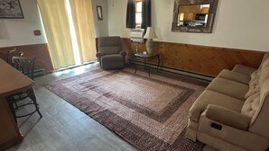 A living room with a ceiling fan, a brown armchair, a beige sofa, a patterned rug, and a dining table with chairs. - Rustic Ridge (Gregory)