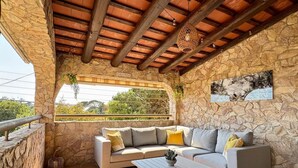 A stone-walled room with a wooden ceiling, a sofa with cushions, a small table, and a hanging light fixture.