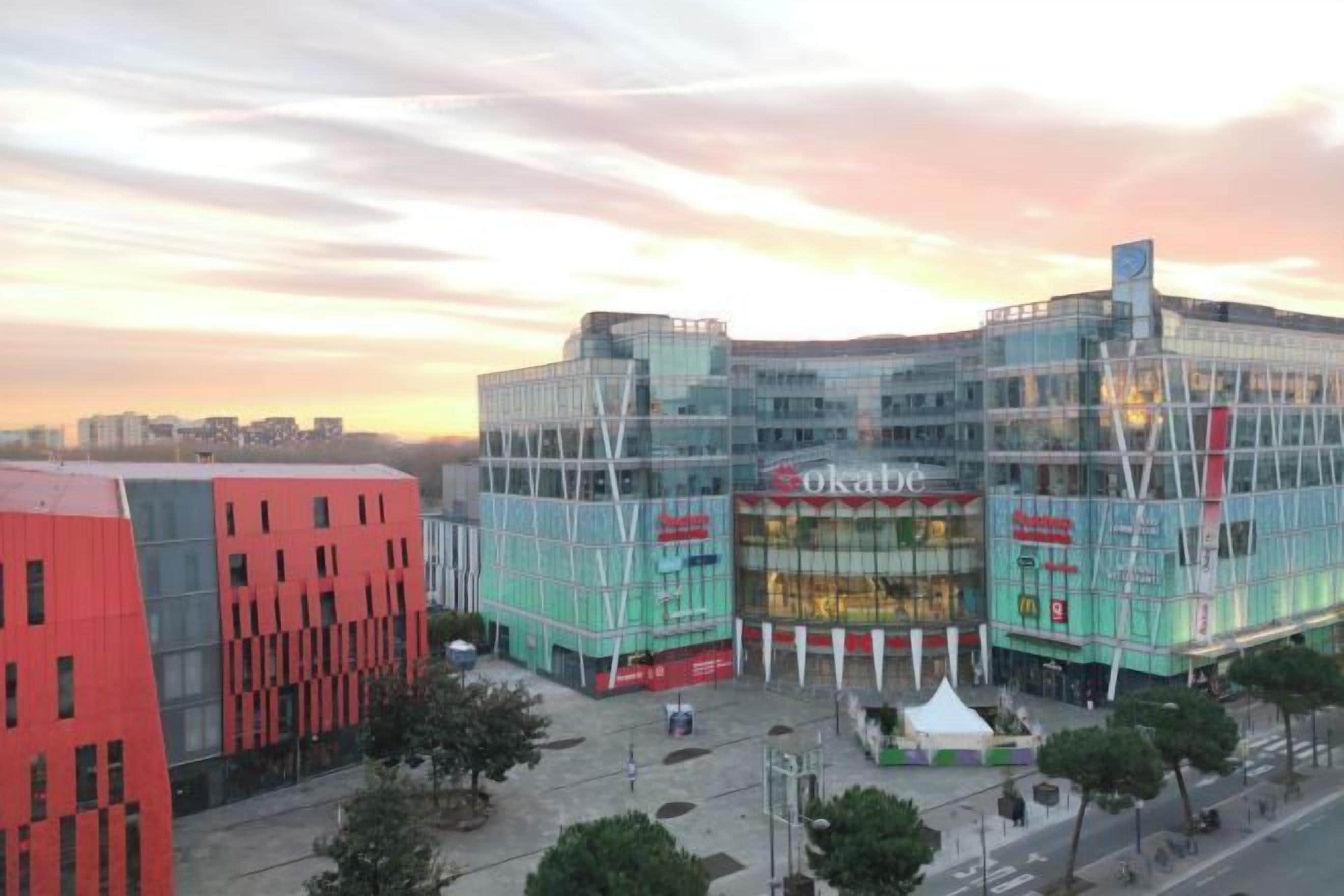 A modern building with a glass facade, a prominent sign, and a red structure to the left.