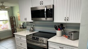 Una cocina moderna con armarios blancos, un microondas de acero inoxidable, horno empotrado y tostadora.