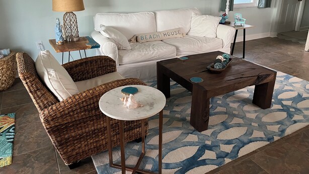 Una sala de estar con un sofá blanco, sillas de mimbre, una mesa de centro y elementos decorativos en la pared.