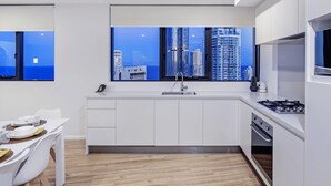 Une cuisine moderne avec vue sur la ville, des meubles blancs, un coin repas avec une table et des chaises, et un four encastré.