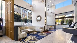 Un hall d’hôtel moderne doté d’un espace salon, d’un comptoir d’accueil et de grandes fenêtres offrant une vue sur la ville.