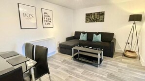 A modern living room with a sofa, a coffee table, and a dining area with chairs. - Warmley Flat by Pulse Properties - close to Bristol Centre, Bath and Cotswolds. (Warmley)