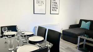 A dining area with a table set for four, chairs, and framed wall art. - Warmley Flat by Pulse Properties - close to Bristol Centre, Bath and Cotswolds. (Warmley)