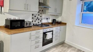 A modern kitchen with white cabinets, a microwave, toaster, kettle, and oven. - Warmley Flat by Pulse Properties - close to Bristol Centre, Bath and Cotswolds. (Warmley)