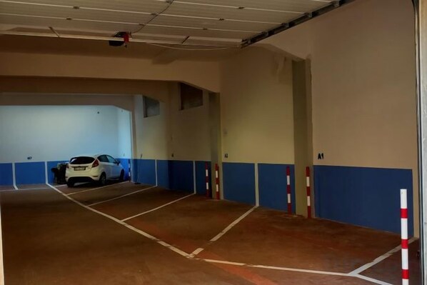 Un garaje para estacionar con espacios delimitados y un coche blanco aparcado en uno de ellos.