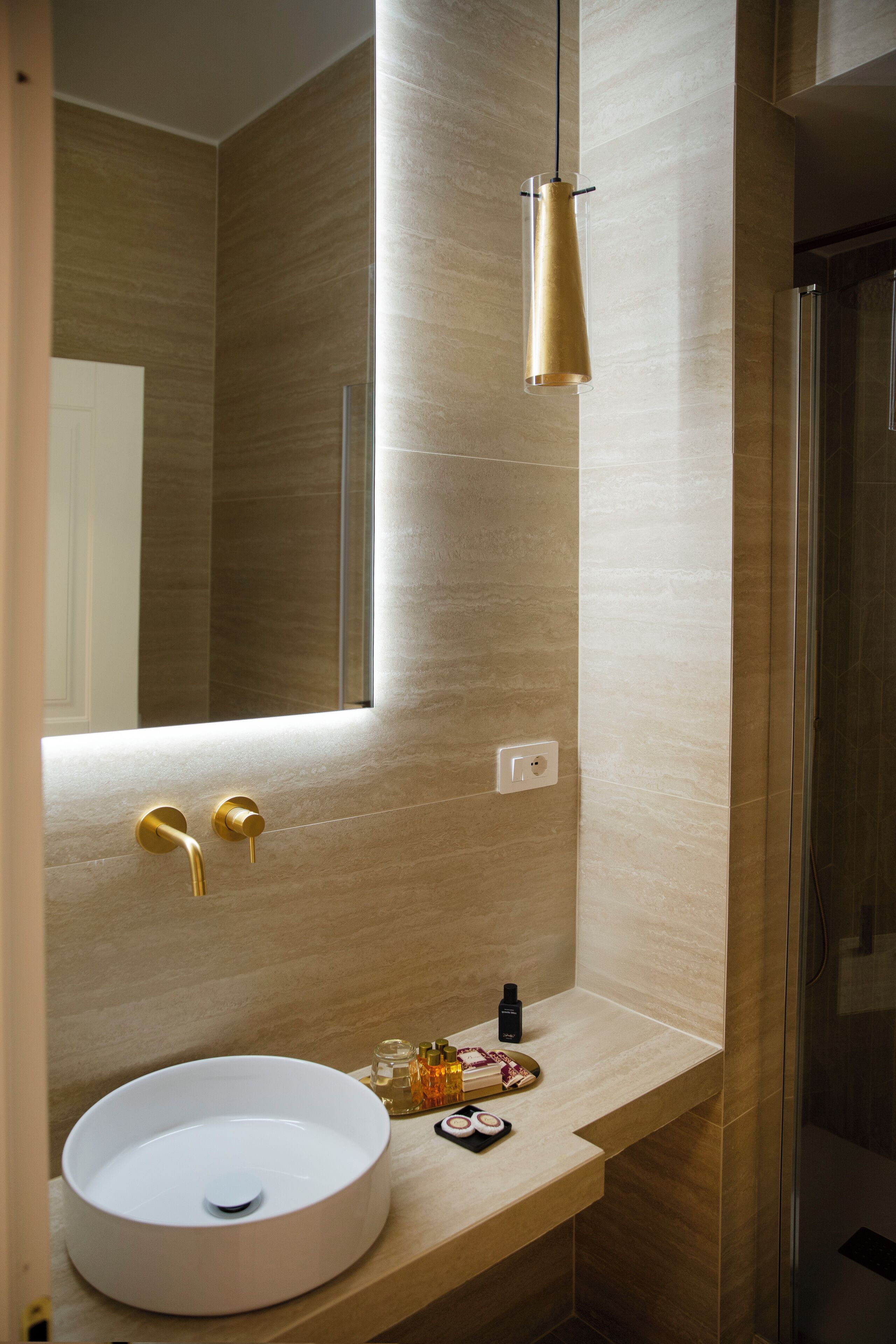 Un baño moderno con un espejo grande, un lavabo redondo y un grifo dorado.