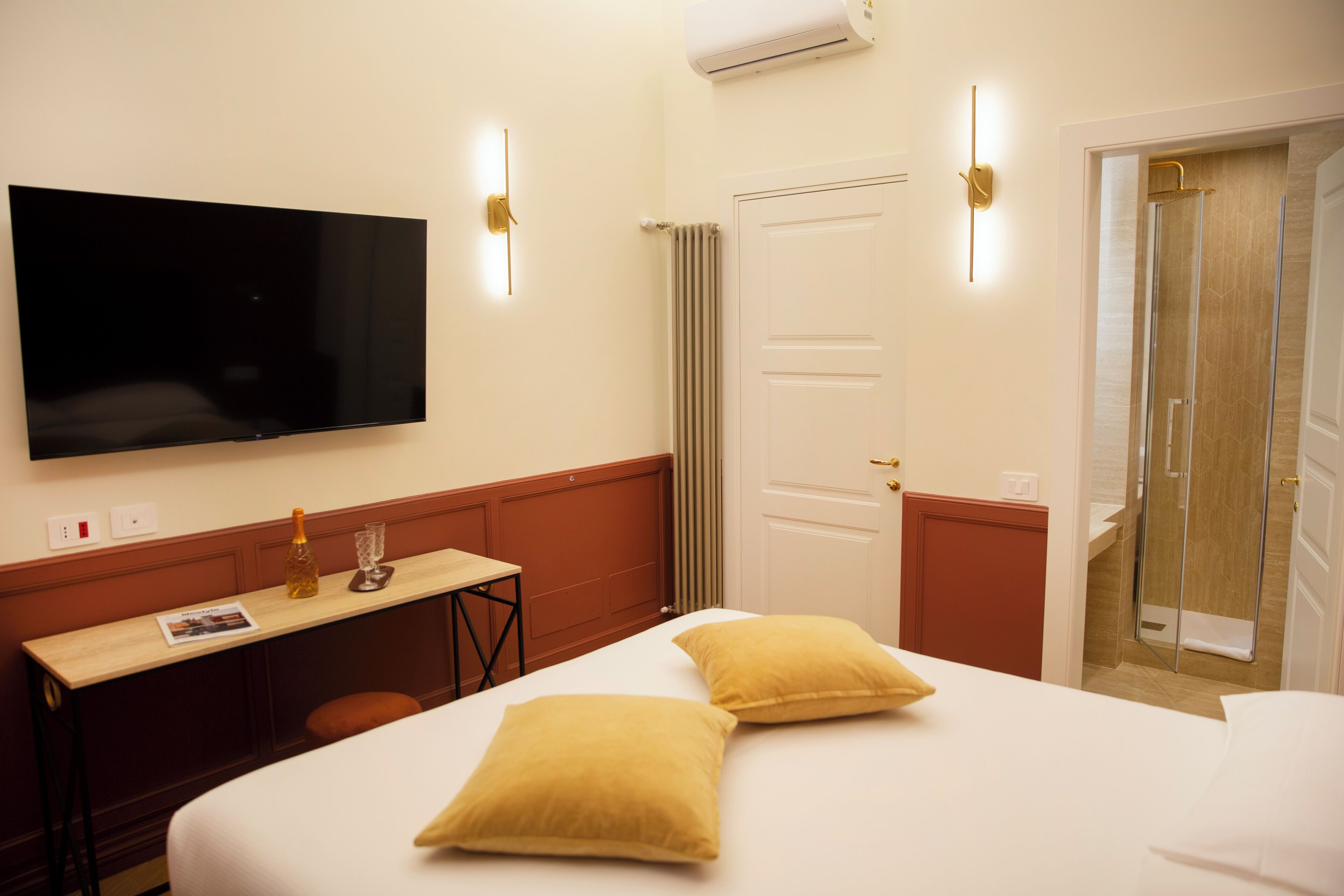 Quarto de hotel com cama, escrivaninha, televisão e chuveiro.