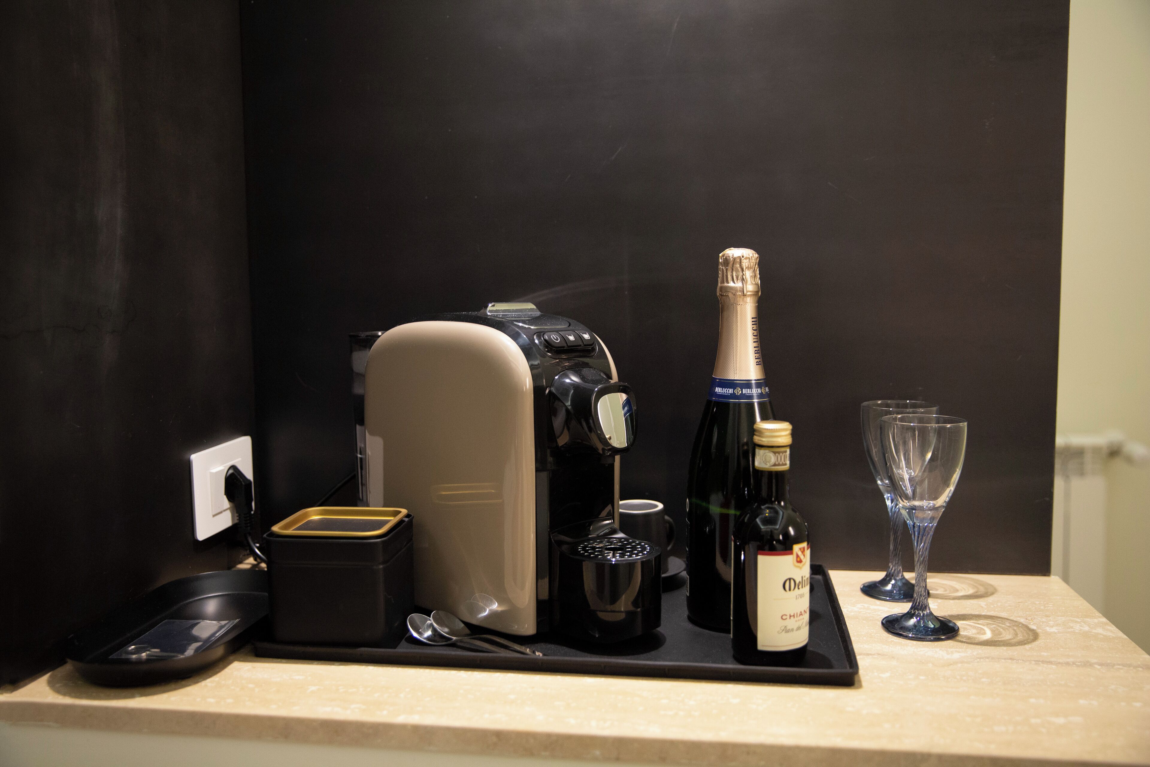 A coffee maker, a bottle of champagne, and two wine glasses on a countertop.