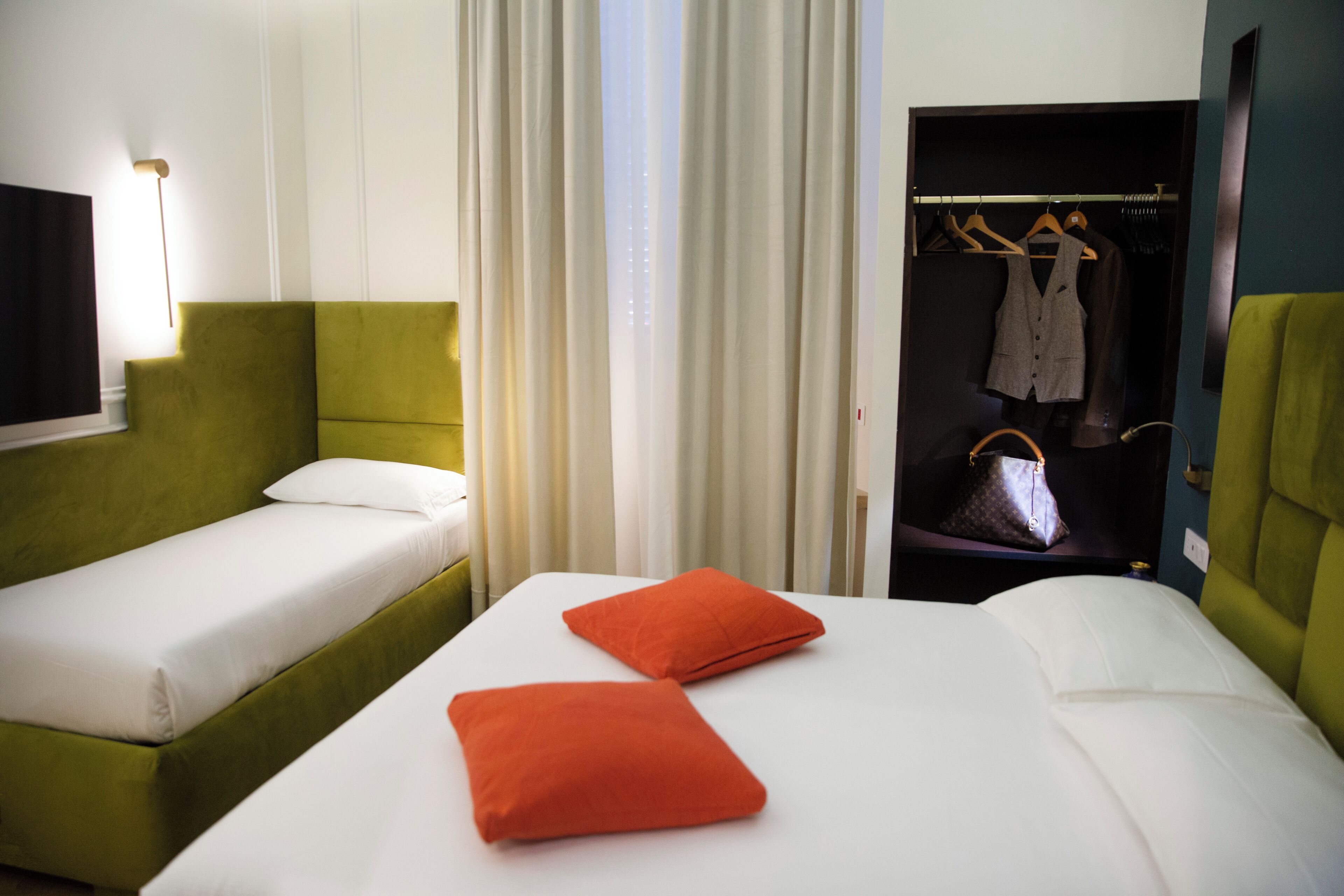 A hotel room with two beds, a green headboard, white bedding, and an open closet with hanging clothes.