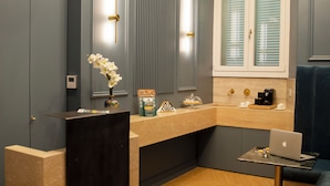 A modern bathroom with a vanity, sink, and mirror. There is a blue bench and a small table with a laptop. - Unicum Trastevere Suites (Rome)