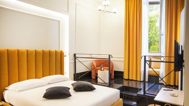 A hotel room with a bed, a small table, a chair, and a TV. - Unicum Trastevere Suites (Rome)