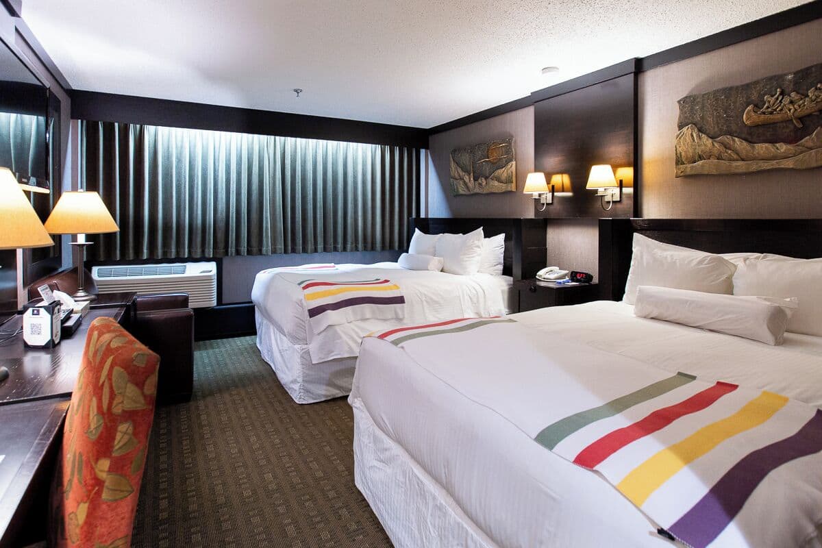 A hotel room with two beds, a desk with a lamp, a chair, and artwork on the walls.