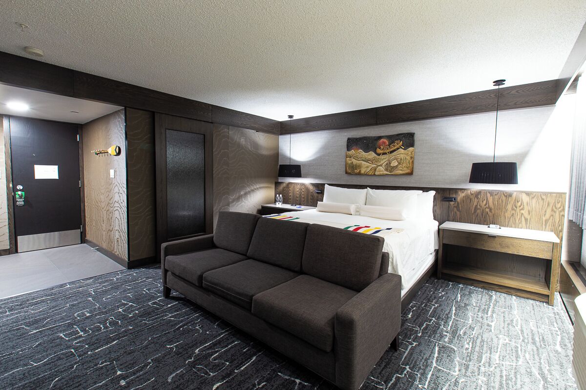 A modern hotel room with a sofa, a bed, a nightstand, and a painting on the wall.
