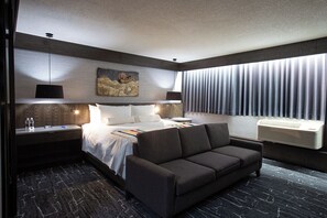 A modern hotel room with a large bed, a sofa, a painting on the wall, and a window with curtains.