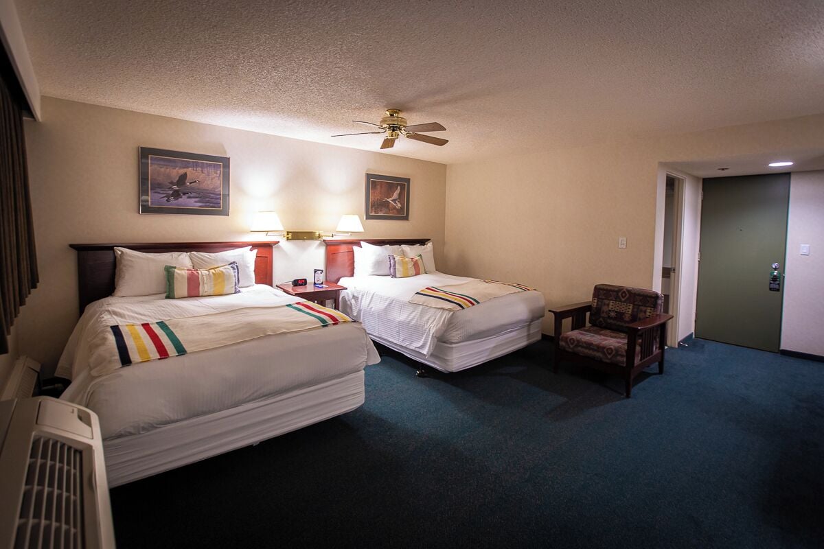 Ein Hotelzimmer mit zwei Betten, einem Sessel, einem Deckenventilator und zwei Wandleuchten.