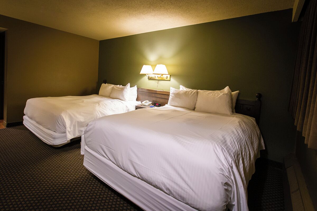 A hotel room with two beds, a nightstand, and a wall-mounted lamp.