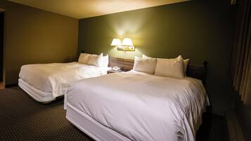 A hotel room with two beds, a nightstand, and a wall-mounted lamp.