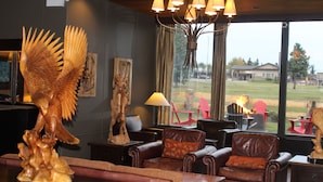 A cozy living room with leather sofas, a wooden sculpture, and a large window overlooking a grassy area. - Grande Cache Hotel (Grande Cache)