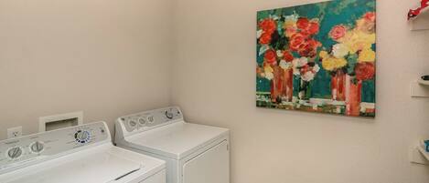 A laundry area with two white dryers and a painting of flowers on the wall.