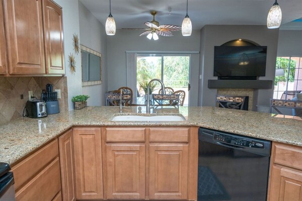A kitchen with granite countertops, wooden cabinets, a dishwasher, a built-in oven, and a ceiling fan.