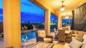 Une terrasse extérieure avec une piscine, des meubles en osier et une vue sur la ville au crépuscule.